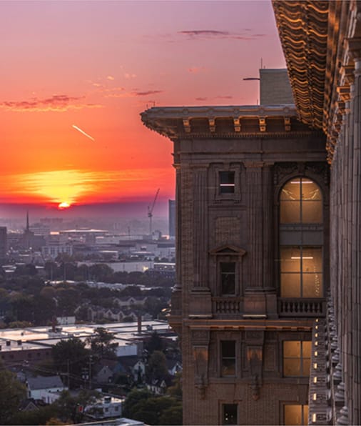 A close-up view of the upper corner of Michigan Central Station at sunset, highlighting its ornate architectural details and tall windows.